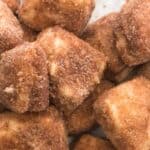 A pile of apple chunks coated in cinnamon sugar on a white background.