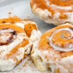 Three cinnamon rolls with white icing and a sprinkle of cinnamon on a plate.