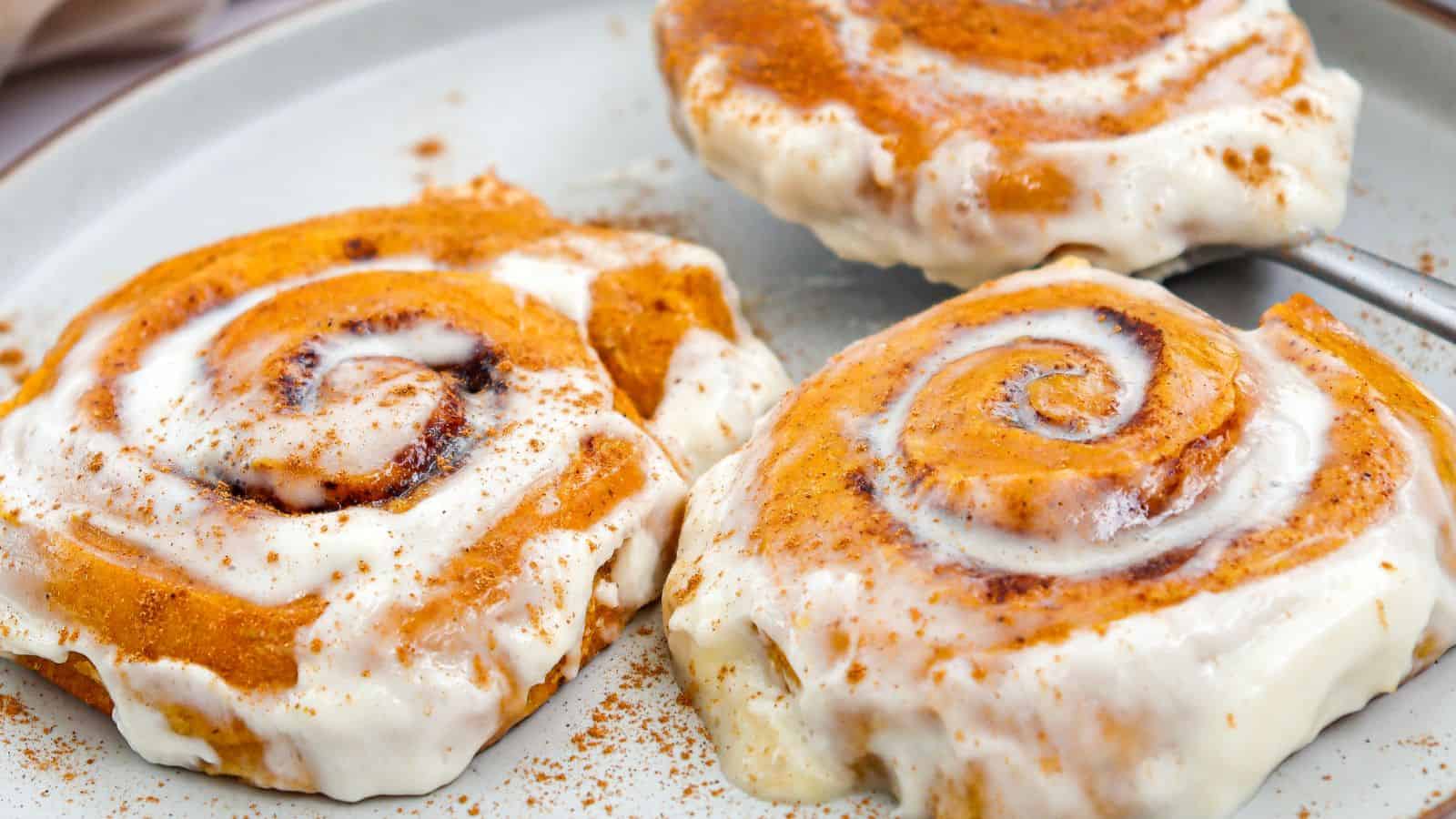 Three cinnamon rolls topped with white icing and sprinkled with cinnamon, served on a plate.