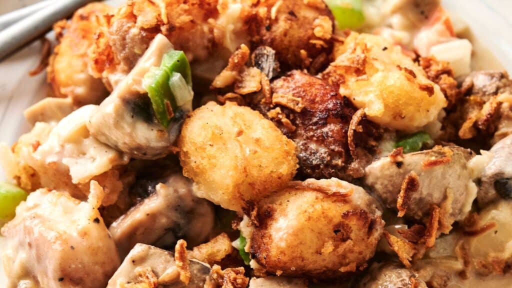 Close-up of a dish featuring crispy tater tots, pieces of green bell pepper, and a creamy sauce, garnished with fried onions.