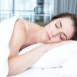 A person sleeping peacefully on a pillow under a white blanket in a bright room.