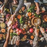 A table brimming with a variety of food, including pumpkins, pomegranates, and dishes being shared by multiple hands, paints the perfect picture of intimate small gatherings and festive cheer.