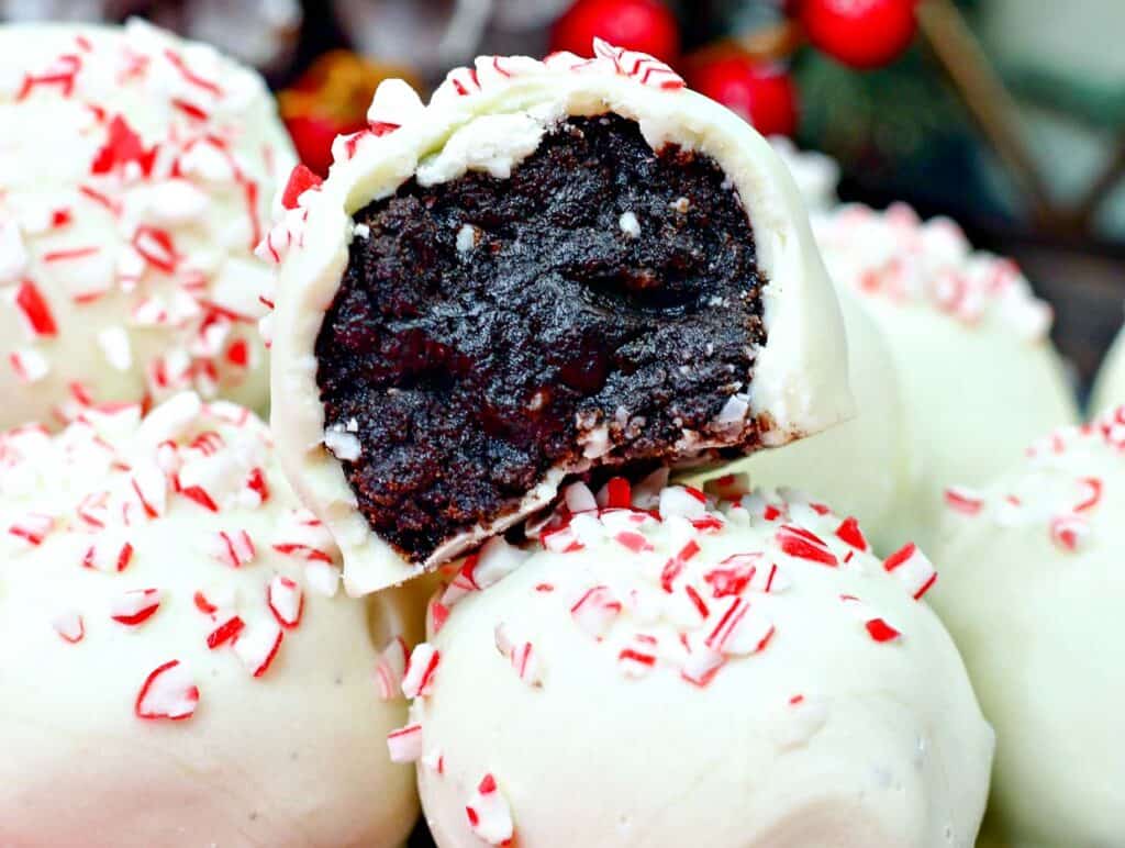 Close-up of white chocolate truffles with crushed peppermint on top. One truffle is cut open, revealing a dark chocolate filling.