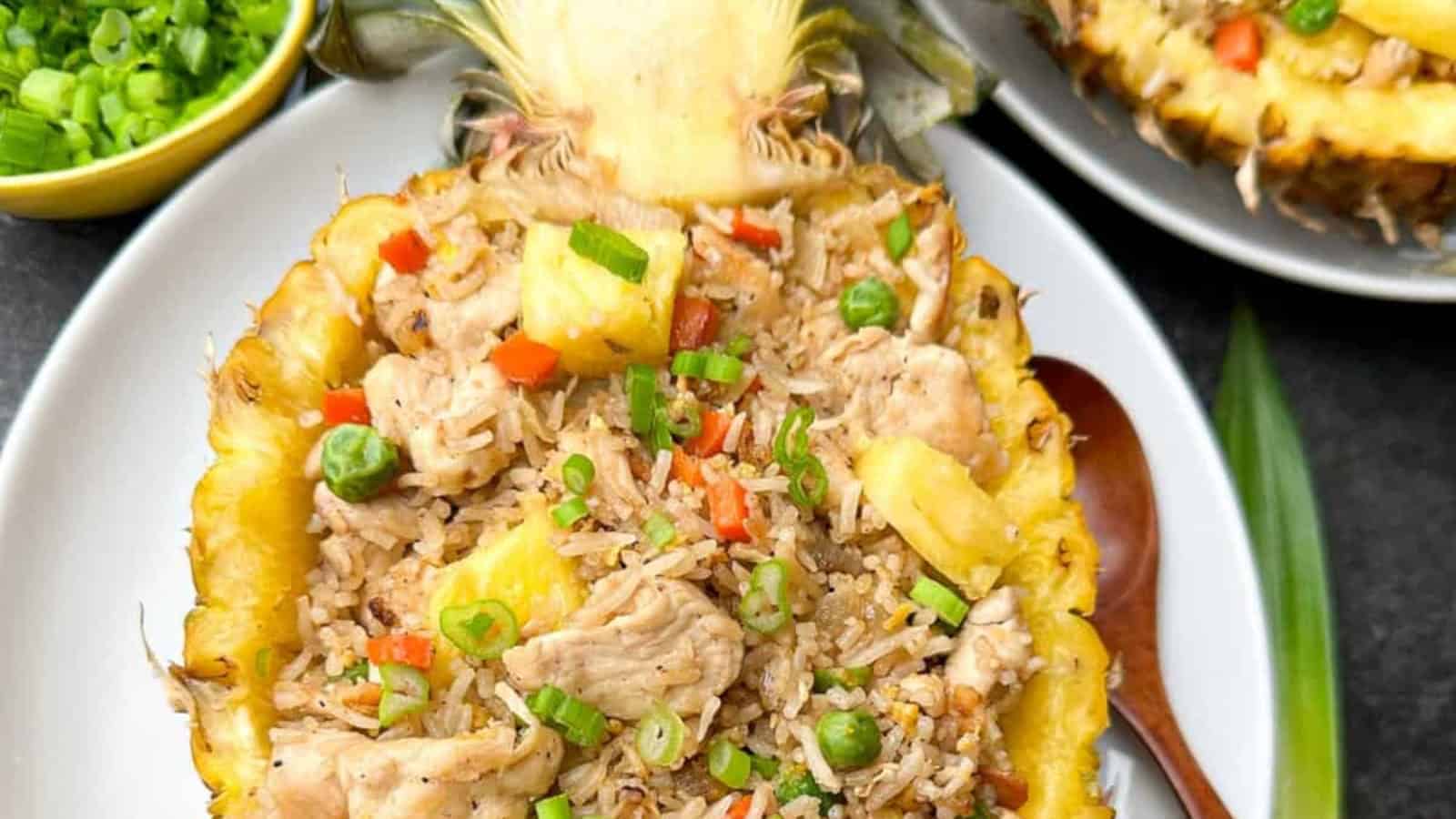 Pineapple half filled with chicken fried rice, peas, and diced red peppers; garnished with green onions.