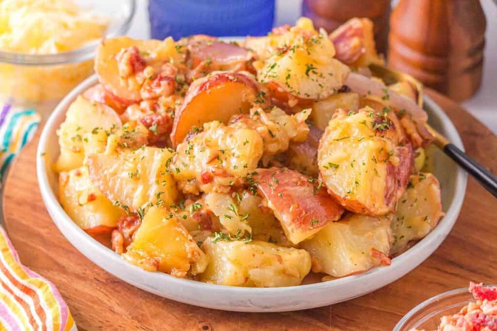 A plate of cheesy baked potatoes with herbs and bacon bits, served on a wooden table.