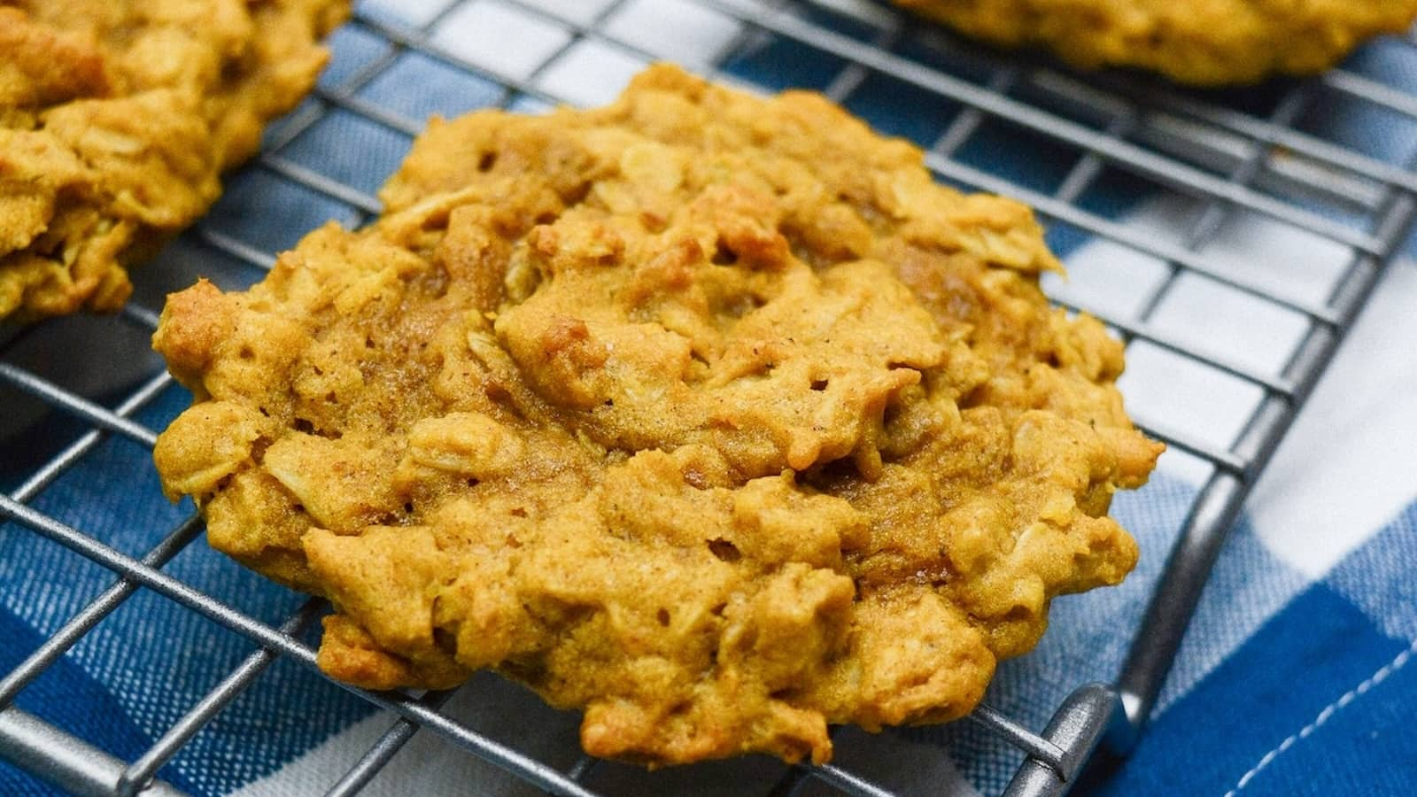 Close-up of homemade pumpkin oatmeal cookies cooling on a wire rack over a blue and white checkered cloth.