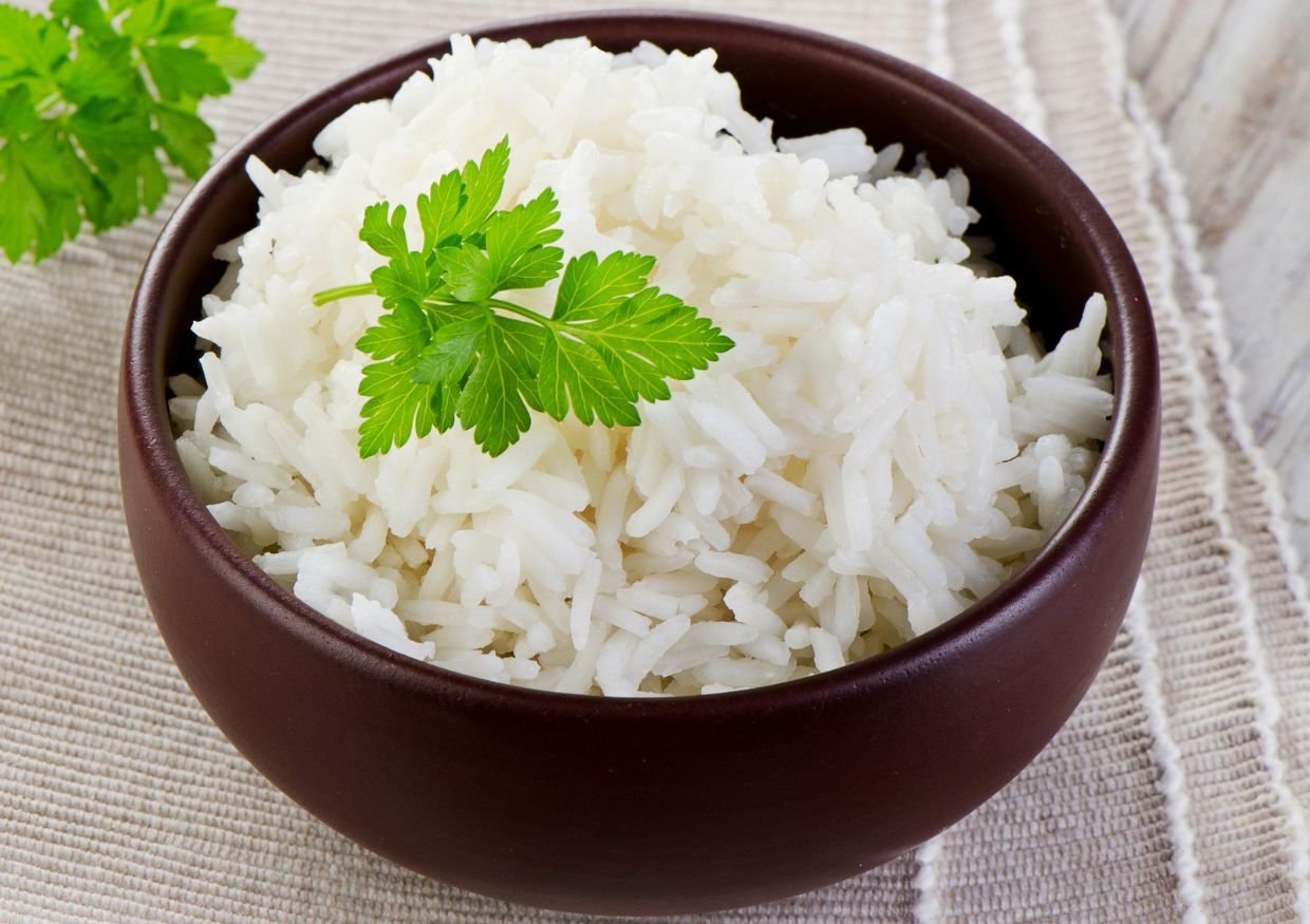 A bowl of cooked white rice garnished with a sprig of parsley, placed on a striped cloth.