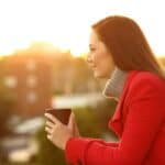 A woman in a red coat holds a mug, gazing into the distance during a sunset, finding solace to help get through the holidays.