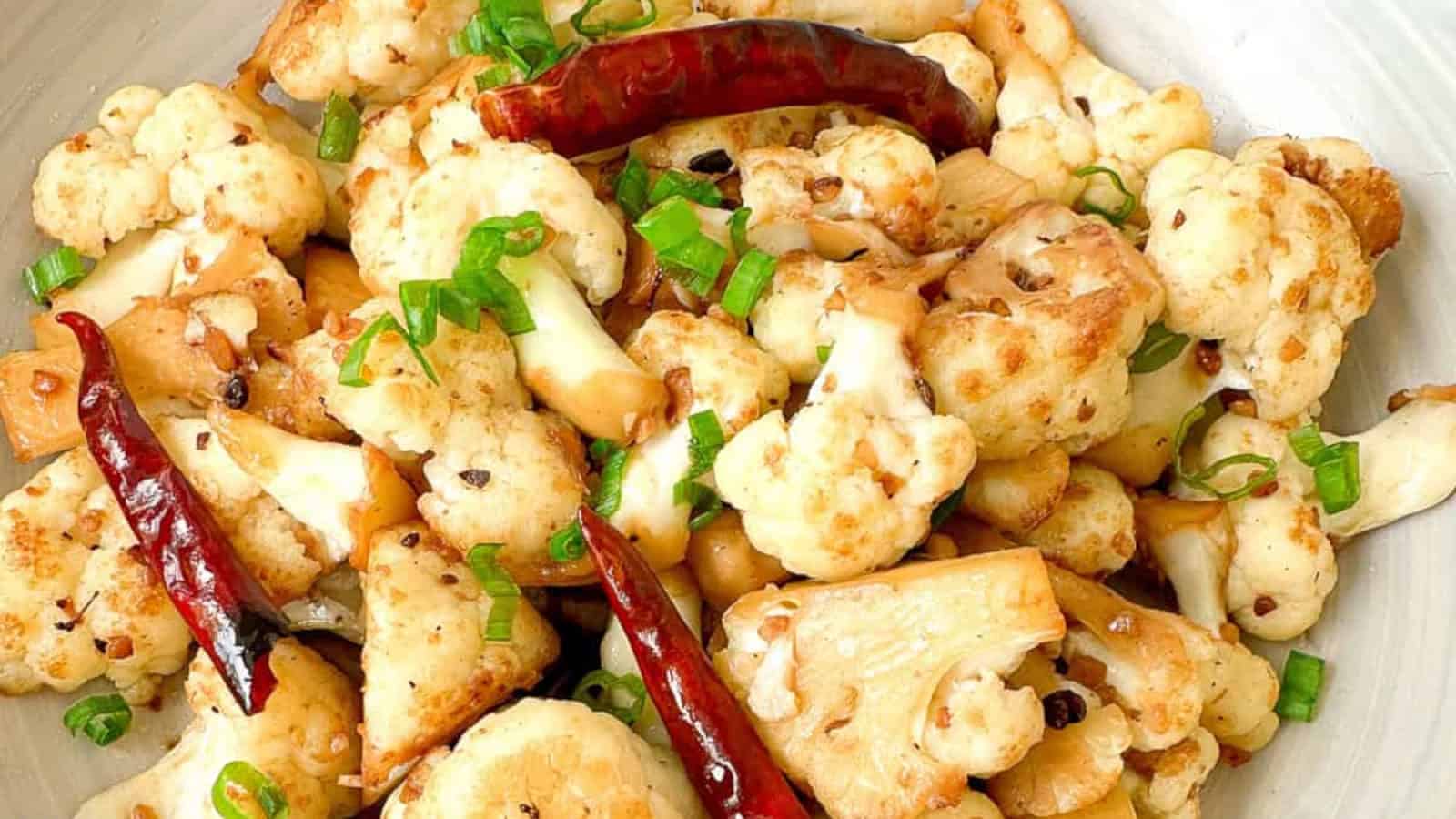Stir-fried cauliflower with mushrooms, dried red chilies, and green onions on a white plate.