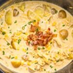 Creamy soup with chicken, potatoes, corn, and cheese in a slow cooker, topped with chopped bacon and green onions.