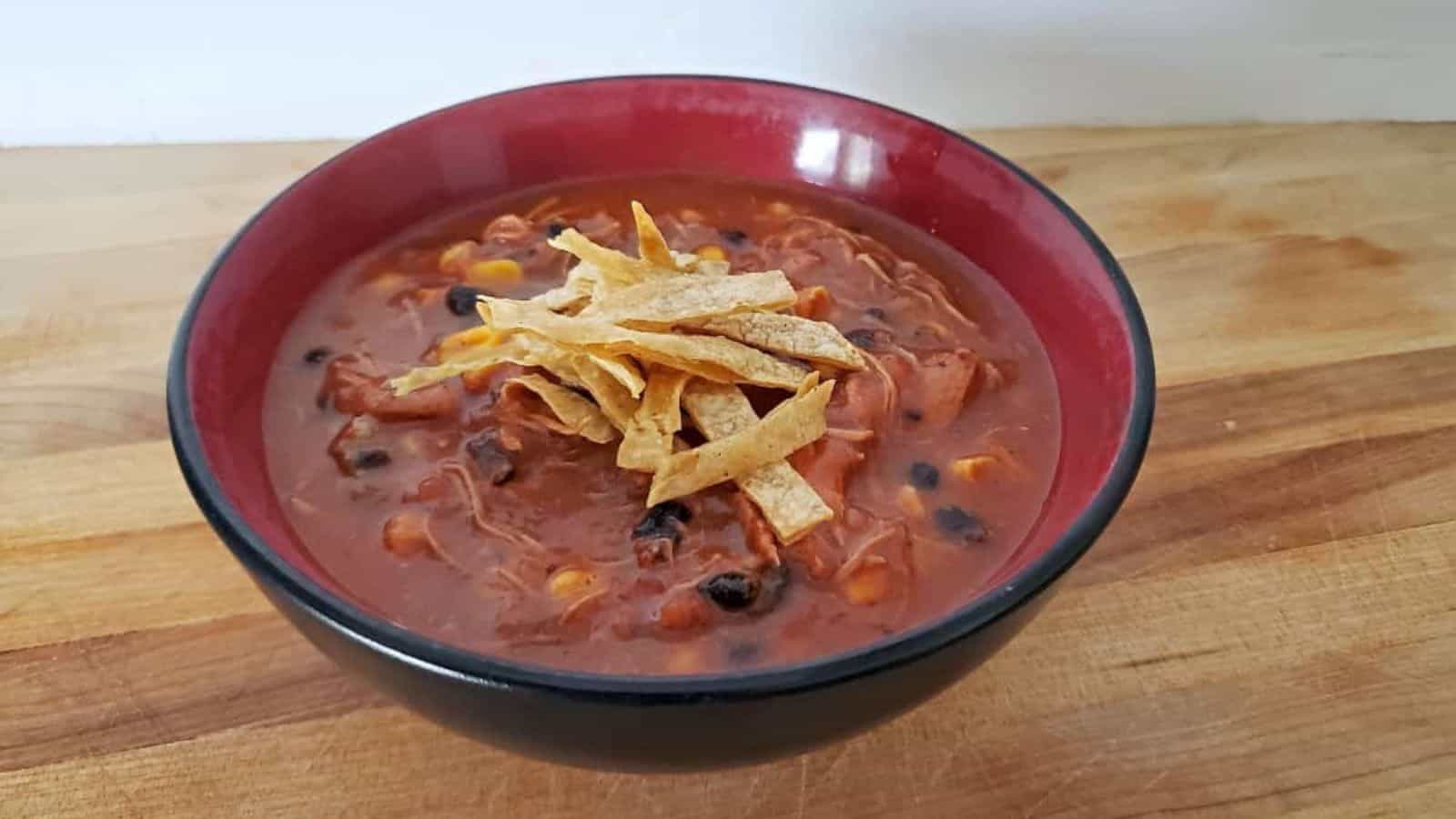 A bowl of chili with black beans, corn, and shredded chicken, topped with crispy tortilla strips.