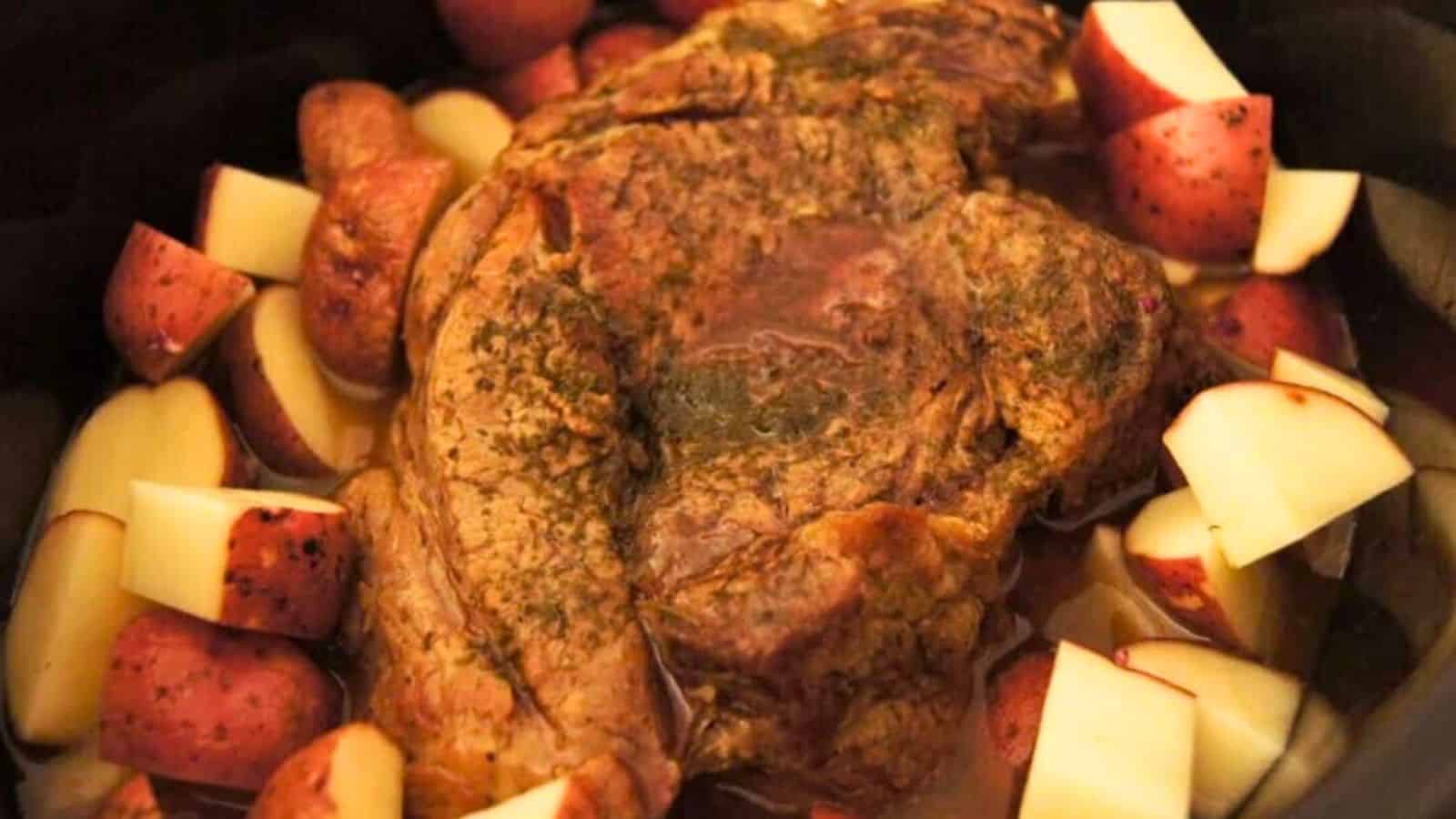 A cooked beef roast surrounded by halved red potatoes in a slow cooker.