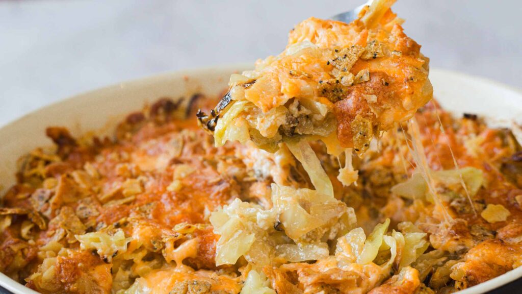 A serving of cheesy, baked pasta with a crispy, golden crust being scooped from a casserole dish.