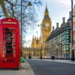 On a bustling street, a classic red telephone booth stands proudly with Big Ben and the Houses of Parliament in the backdrop, capturing the essence of London—a perfect start for memorable day trips from London.