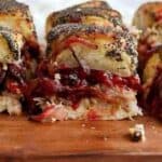 Close-up of sliced turkey sliders with poppy seed crust, filled with cranberry sauce and cheese, displayed on a wooden board.