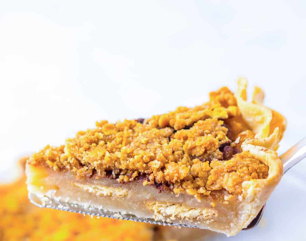 A slice of pie with a crumbly topping on a fork, against a light background.