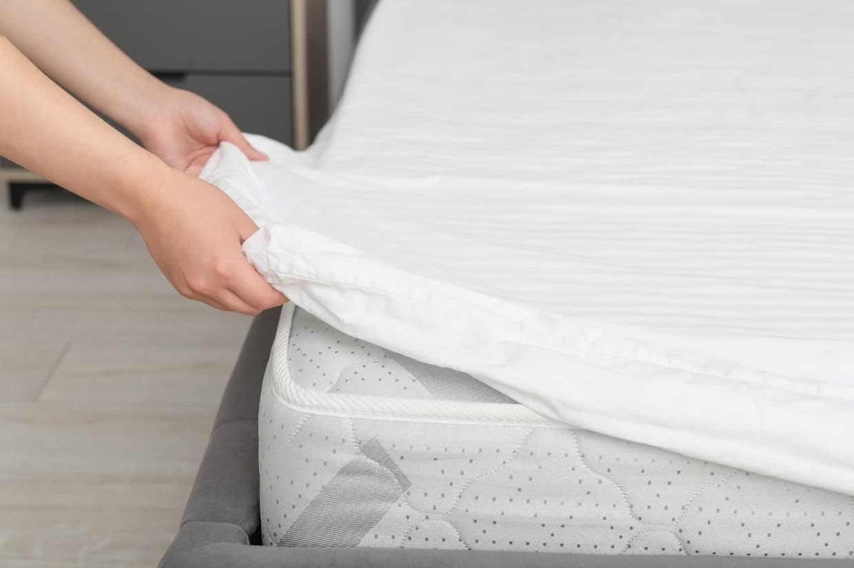 A person carefully adjusts a white sheet on a mattress, demonstrating the first step in mastering how to clean a mattress effectively.