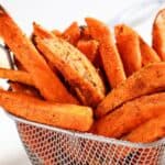 A basket of seasoned sweet potato fries with a small bowl of ketchup in the background.