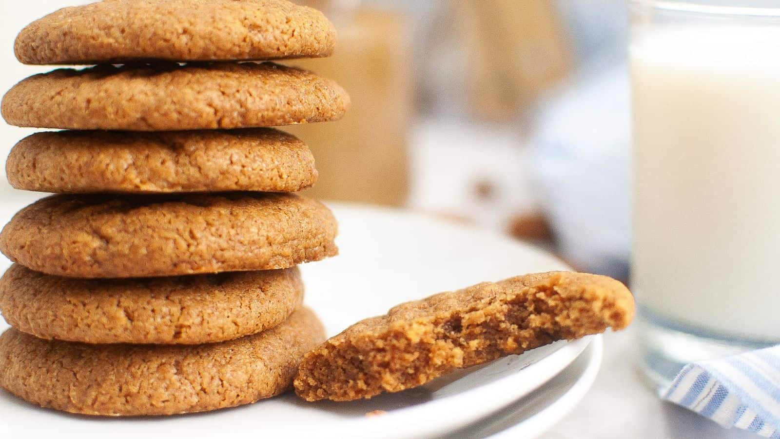 A stack of round cookies on a plate with one cookie partially eaten. A glass of milk is in the background.