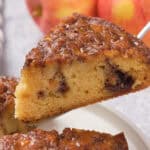 A slice of moist apple cinnamon cake with chocolate chunks is lifted from a whole cake.