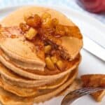 A stack of applesauce pancakes topped with caramelized apple pieces on a white plate.