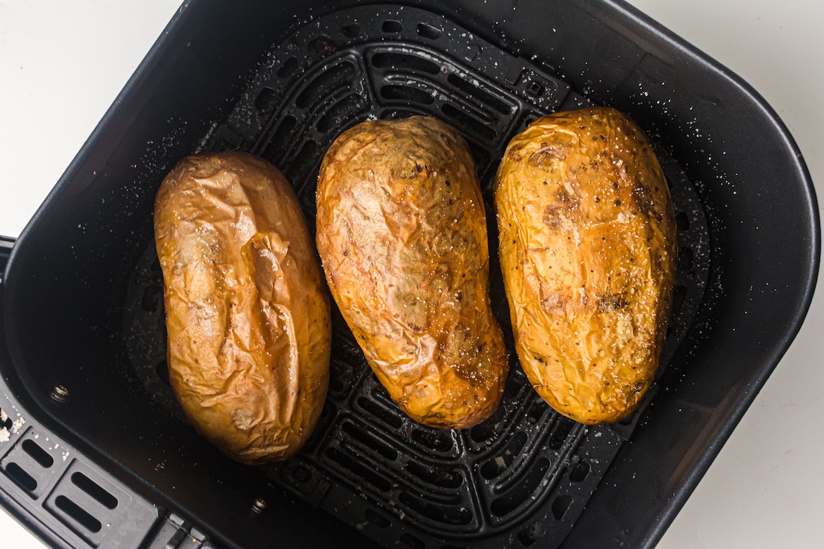 Three baked potatoes with seasoned skin in an air fryer basket.