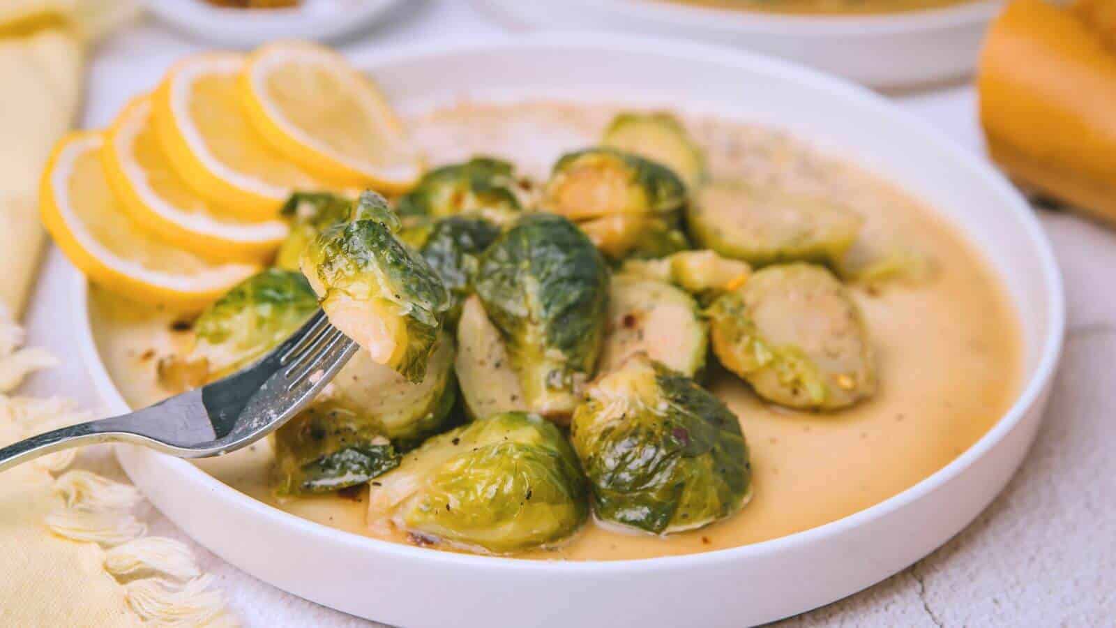 Plate of roasted Brussels sprouts with lemon slices, served with a creamy sauce. A fork holds one sprout above the dish.