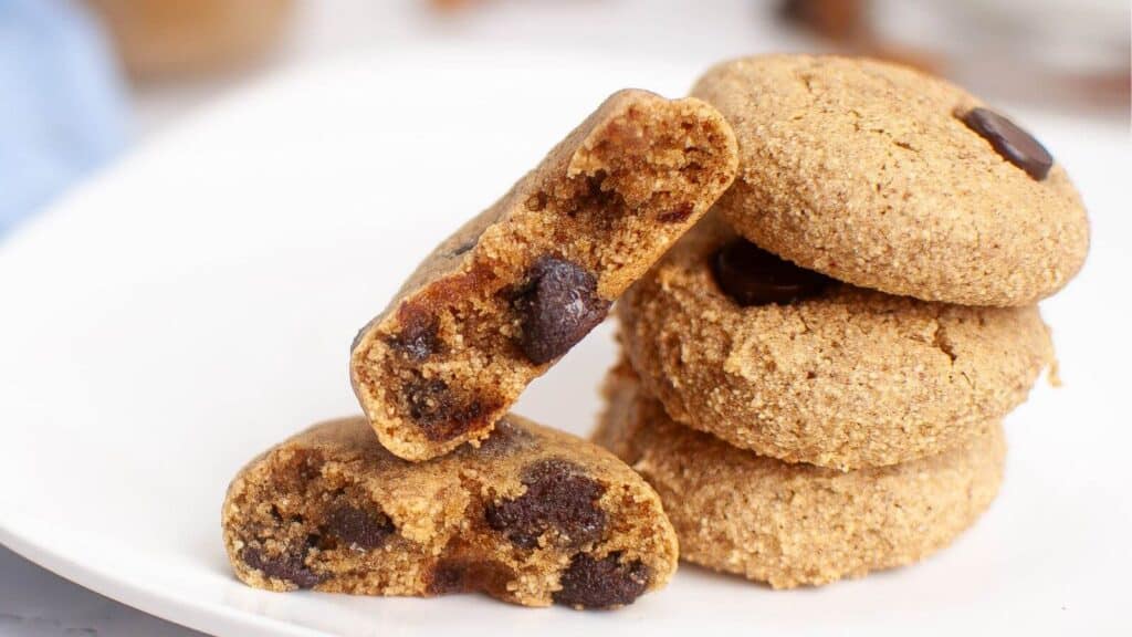 A stack of chocolate chip cookies on a white plate, with one cookie broken in half to show the chocolate chips inside.