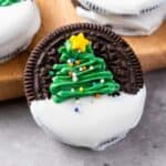 Christmas Oreo, featuring a green frosting Christmas tree and colorful sprinkles, rests on a wooden board.