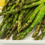 Close-up of roasted asparagus spears on a white plate, garnished with sea salt and a lemon wedge.