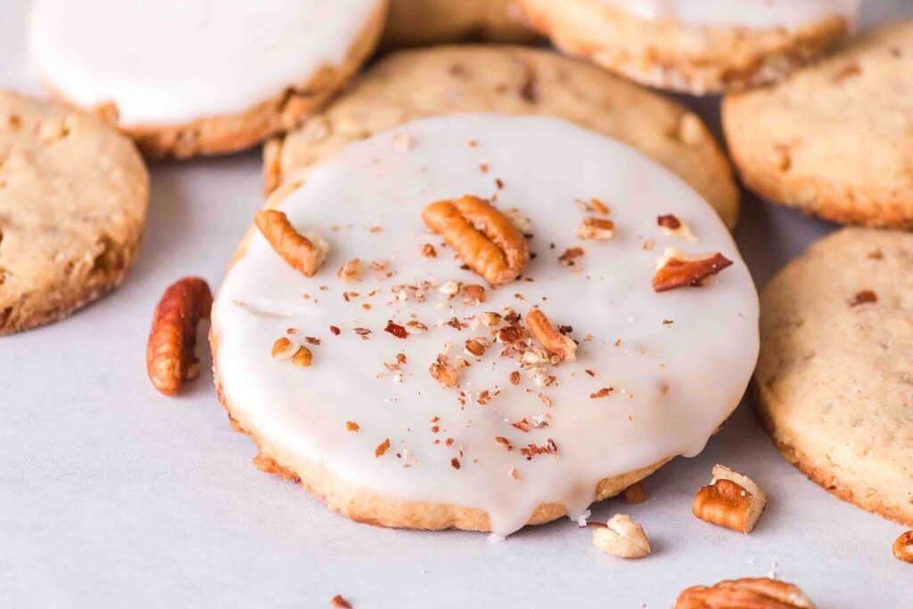 Iced cookies topped with pecan pieces on a white surface.