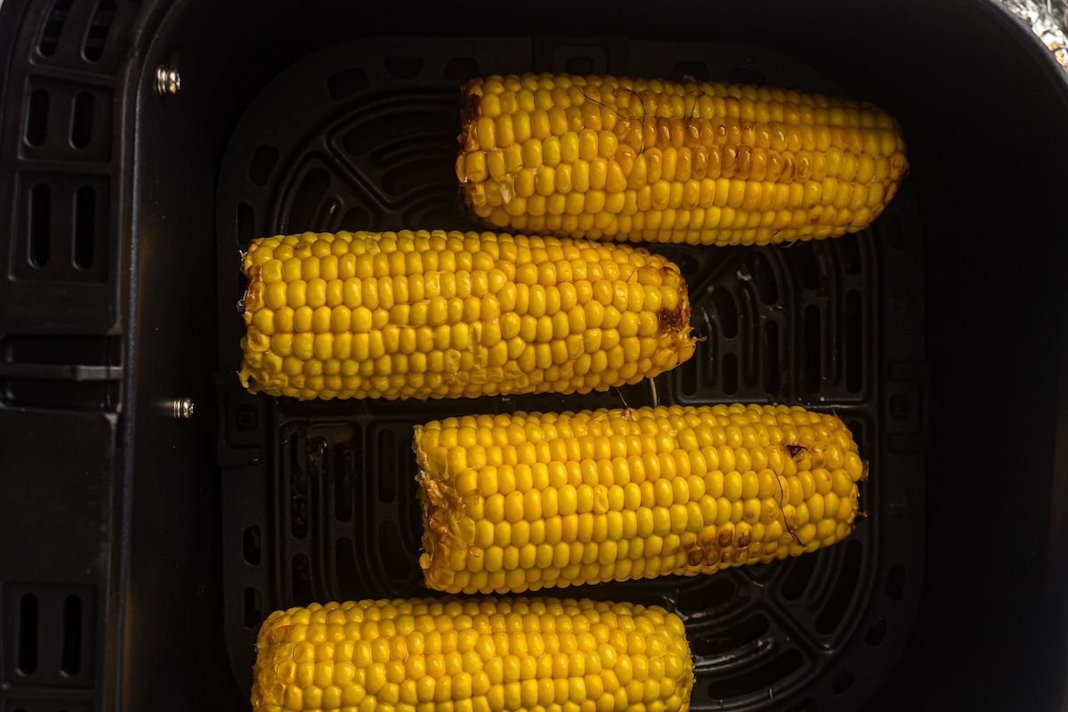 Four ears of corn in an air fryer basket.