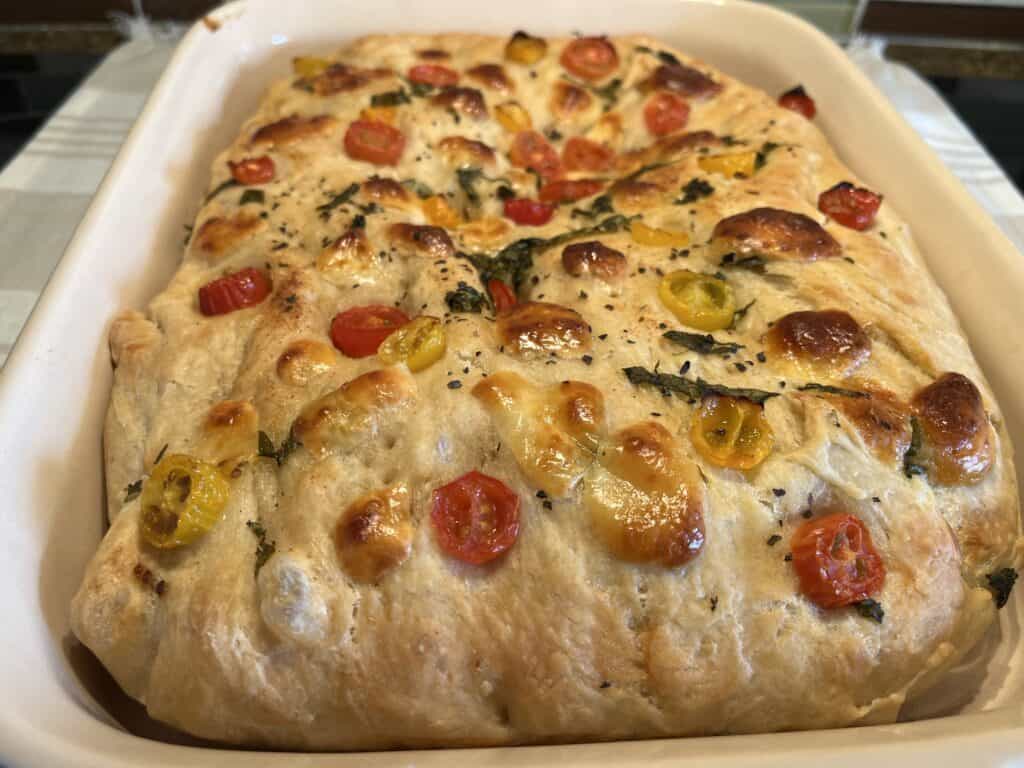 Freshly baked focaccia with cherry tomatoes and herbs in a rectangular baking dish.