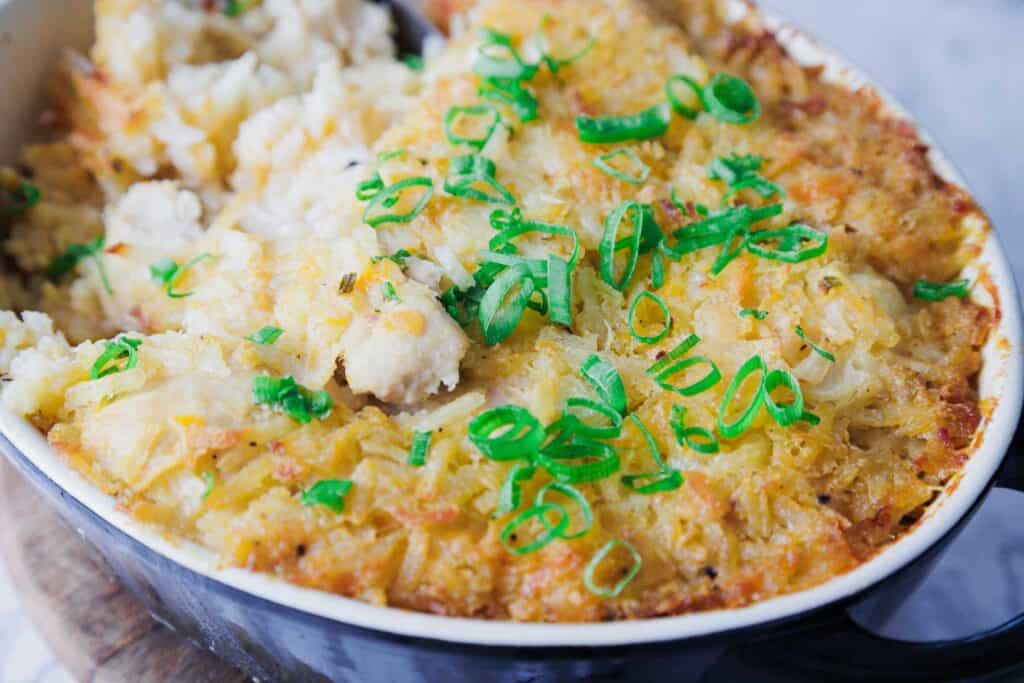 Baked casserole topped with golden cheese and sliced green onions in a black dish.