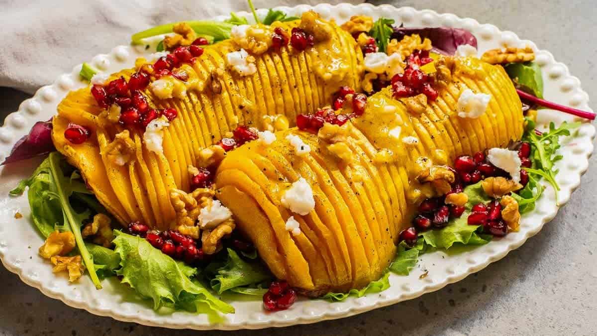 Sliced roasted butternut squash topped with pomegranate seeds, crumbled cheese, and nuts.