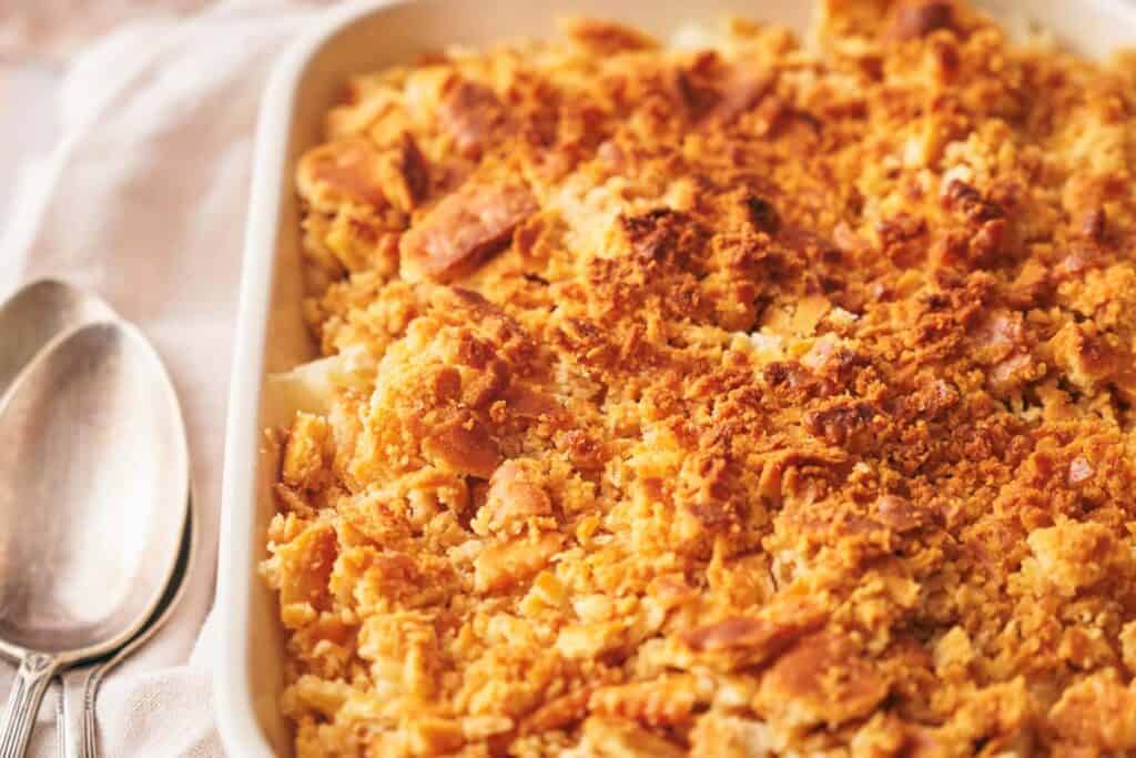 A close-up of a baked casserole with a golden, crispy breadcrumb topping in a rectangular dish. Two spoons are placed beside the dish.