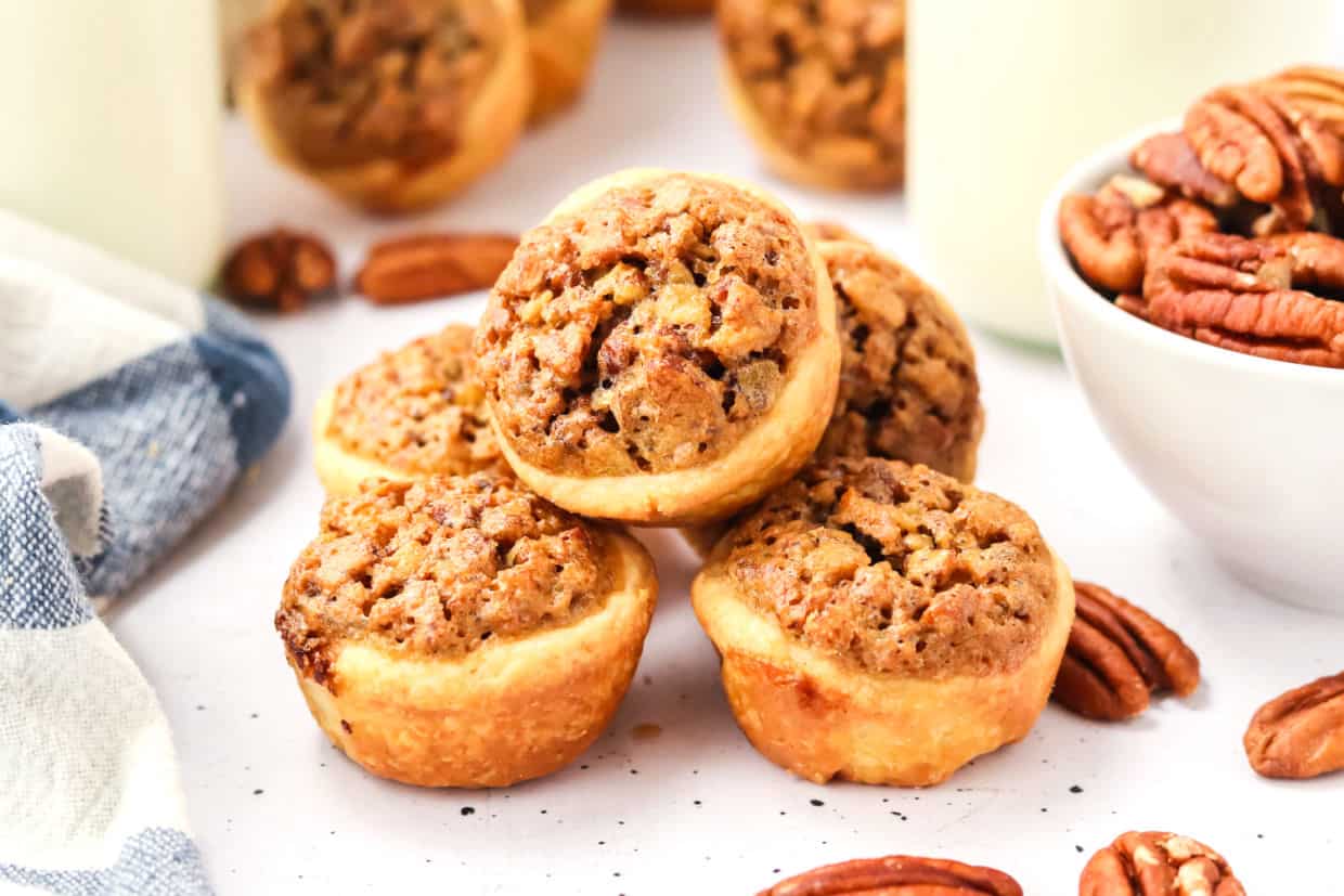 A cup of tea next to a plate of cookies with pecans.