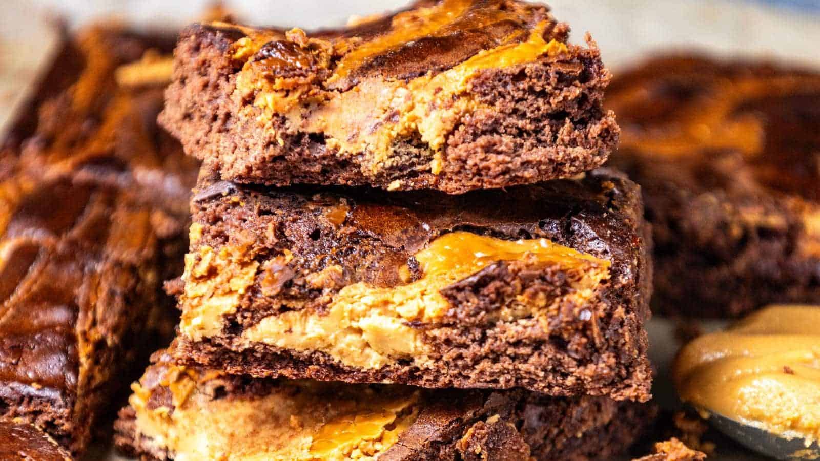 Stack of peanut butter brownies with creamy peanut butter visible in the background.