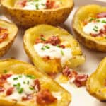 A plate of potato skins topped with melted cheese, sour cream, bacon bits, and chopped chives.