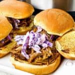 Pulled pork sandwiches with coleslaw on a tray, featuring toasted buns and a background of a stainless steel appliance.