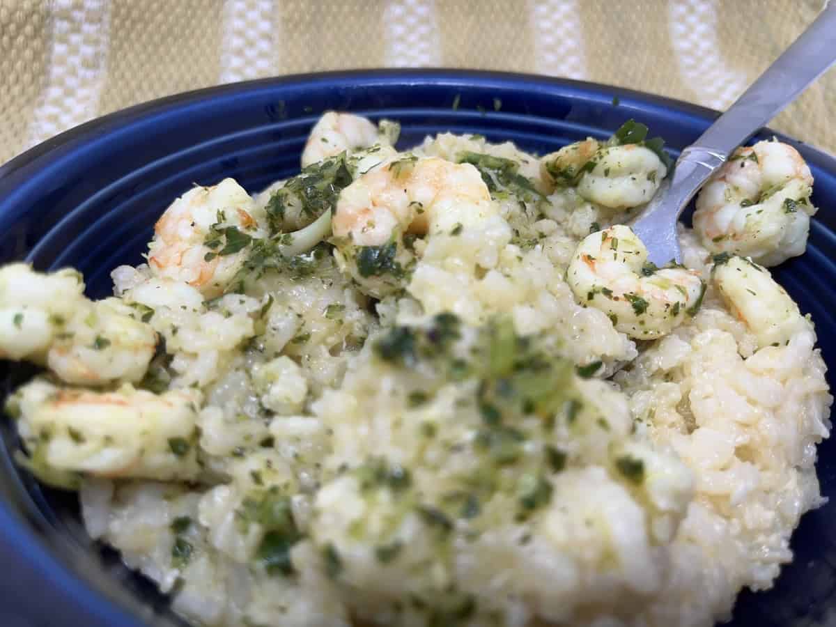 A bowl of creamy risotto with shrimp, topped with green herbs, and a spoon resting on the side.