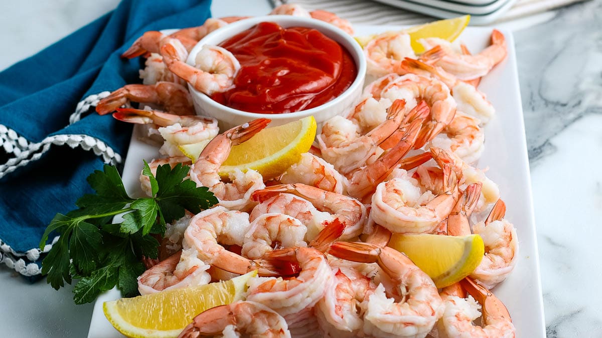 A white platter filled with shrimp cocktail, lemon wedges, and a bowl of cocktail sauce.