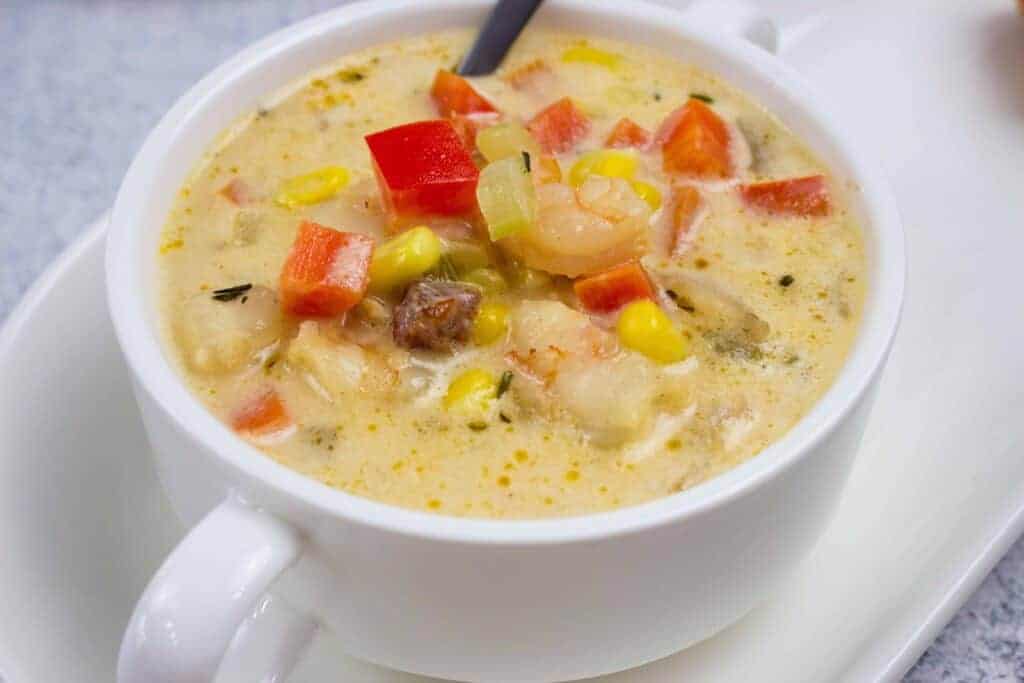 A white bowl of creamy shrimp & corn chowder on a white plate.