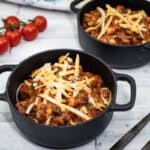 Two black pots of Slow Cooker Southwestern Chili topped with shredded cheese.