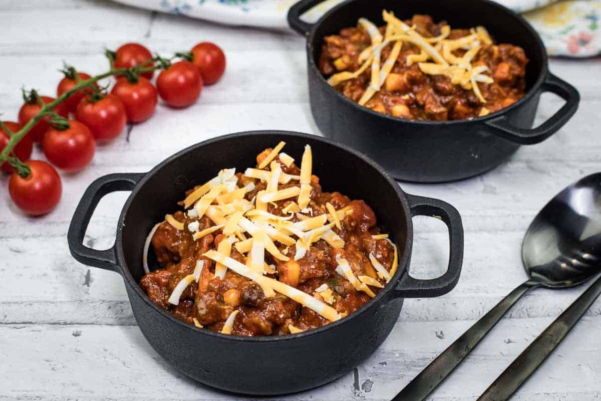 Two black pots of Slow Cooker Southwestern Chili topped with shredded cheese.