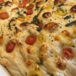 Close-up of homemade focaccia bread topped with cherry tomatoes and herbs, baked to a golden brown.