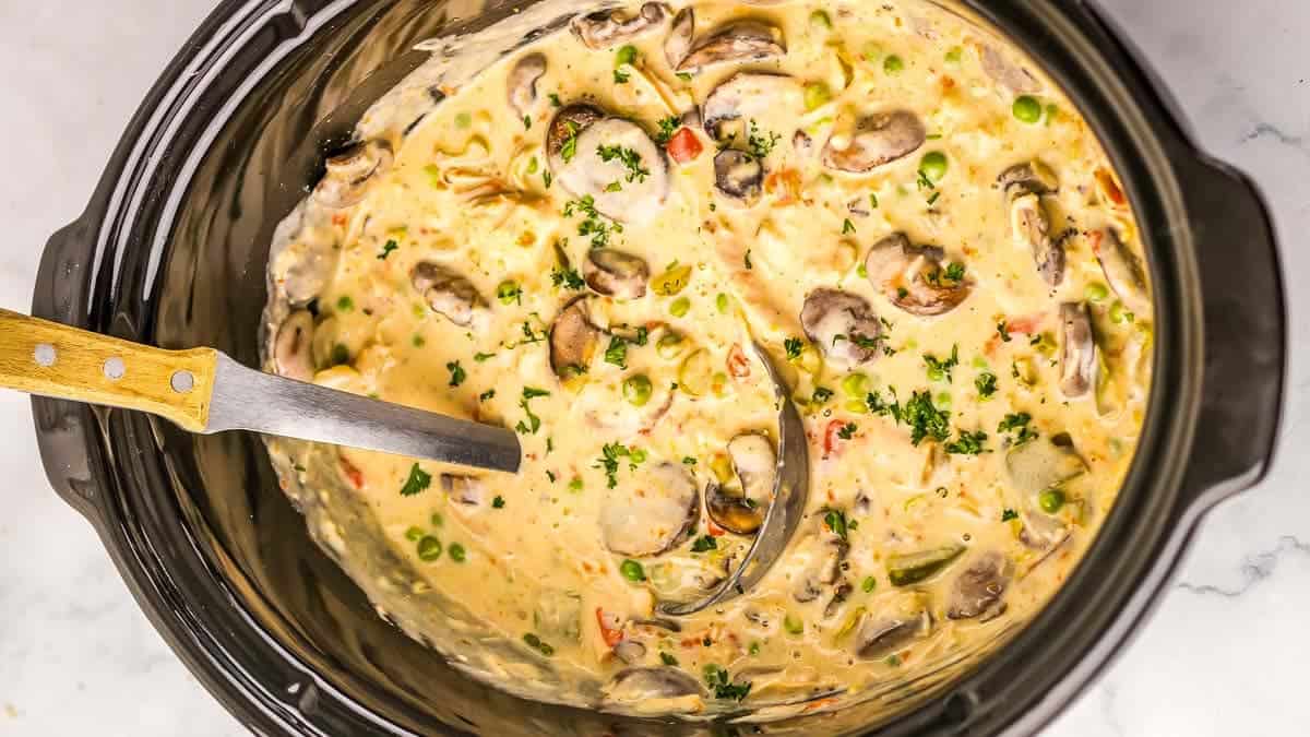 A creamy dish with turkey, mushrooms, peas, and carrots in a slow cooker.