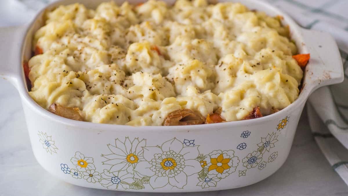 A casserole dish filled with baked shepherd's pie, topped with mashed potatoes and sprinkled with black pepper. The dish has a floral pattern on the side.