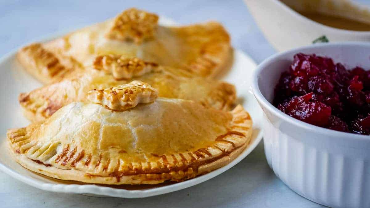 Three thanksgiving hand pies next to gravy and cranberry sauce.