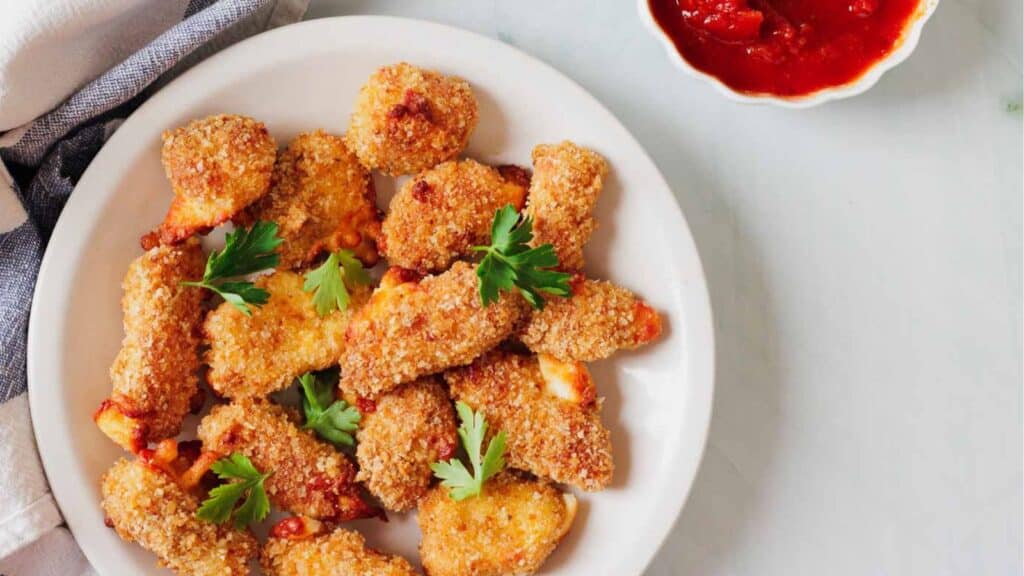 A plate of breaded mozzarella sticks garnished with parsley, next to a small bowl of marinara sauce.